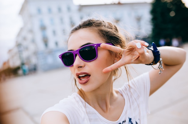 Beautiful young girl in sunglasses showing two fingers, peace gesture