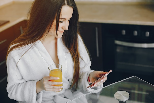 Free photo beautiful young girl with black hair and white robe sitting at home in the kitchen at the table