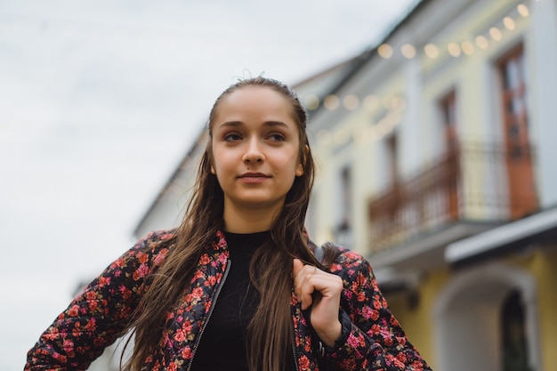 Beautiful young happy brunette girl with long hair posing outdoors. Street photo, portrait, close-up.