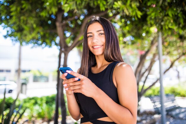 Beautiful young happy latin woman texting on mobile phone on city street. Student girl walking and texting on cell phone outdoors on city street at winter time.