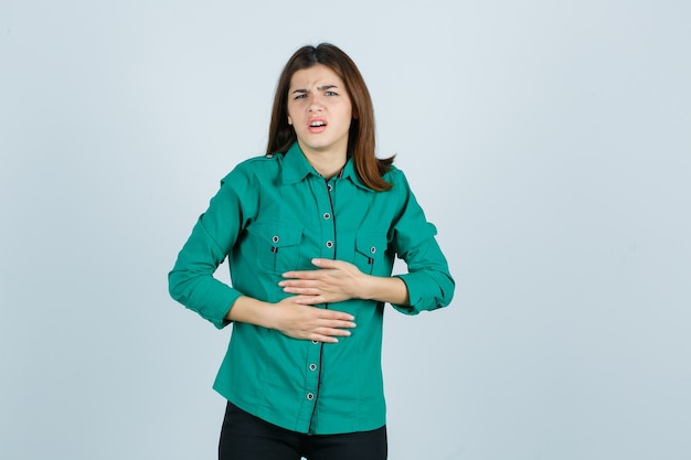 Free photo beautiful young lady in green shirt feeling stomach pain and looking unwell , front view.