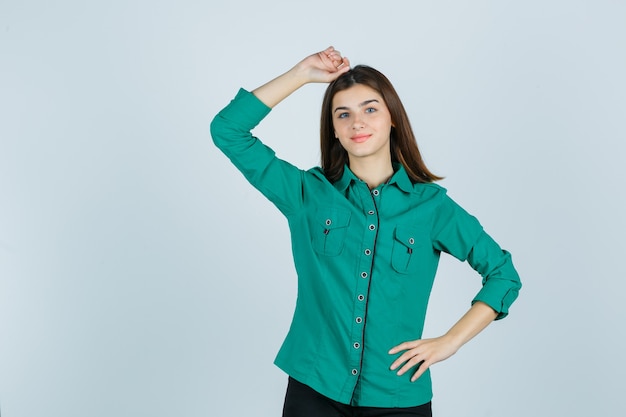 Beautiful young lady holding hand on head in green shirt and looking confident , front view.