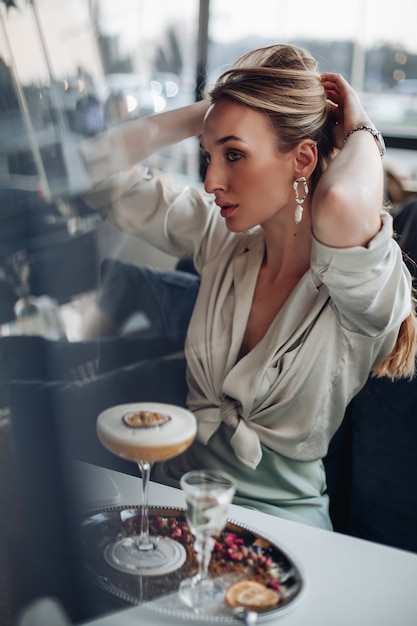 Free Photo beautiful young lady holding her blonde hair and making a pony tail before brakfast in cafe