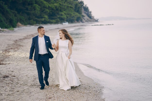 beautiful young long-haired bride in white dress with her young husband on the beach