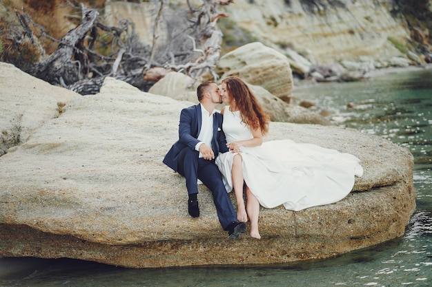 beautiful young long-haired bride in white dress with her young husband near river