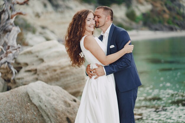 beautiful young long-haired bride in white dress with her young husband near river