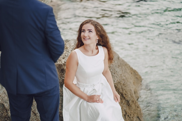 Free Photo beautiful young long-haired bride in white dress with her young husband near river