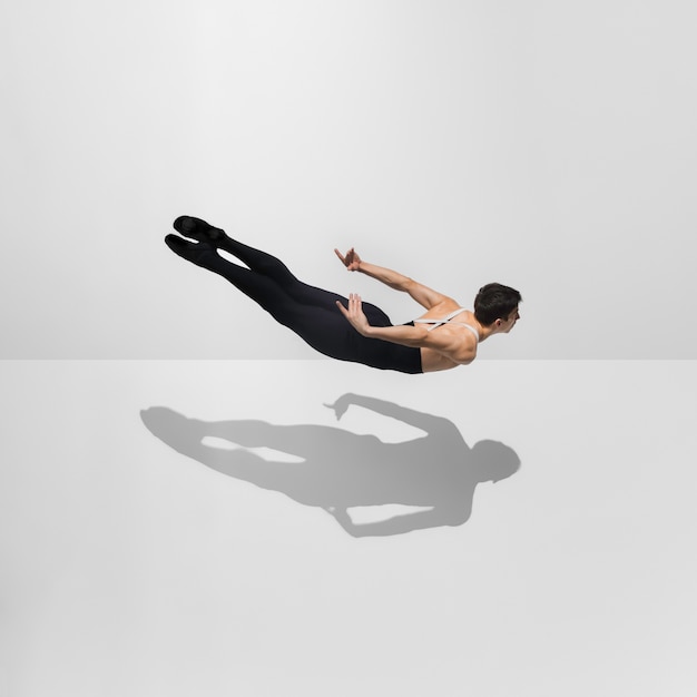 Free Photo beautiful young male athlete practicing on white studio with shadows in jump, air flying