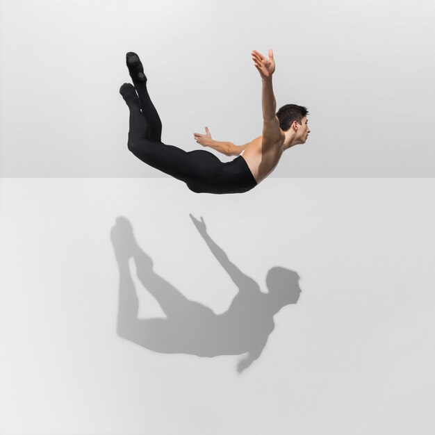 Beautiful young male athlete practicing on white  with shadows in jump, air flying