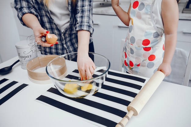 A beautiful young mother with her little daughter is cooking in the kitchen at home