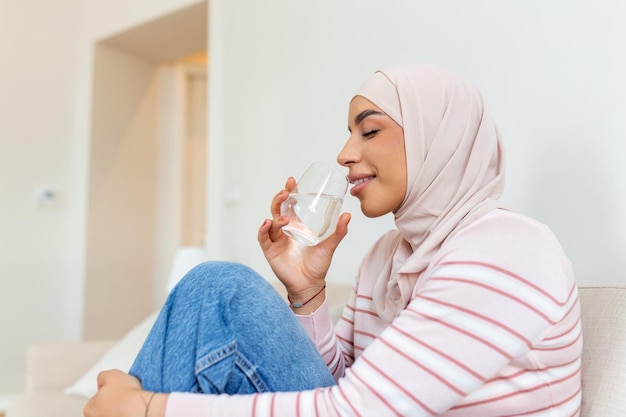 Beautiful young muslim woman with hijab drinking a fresh glass of water at home