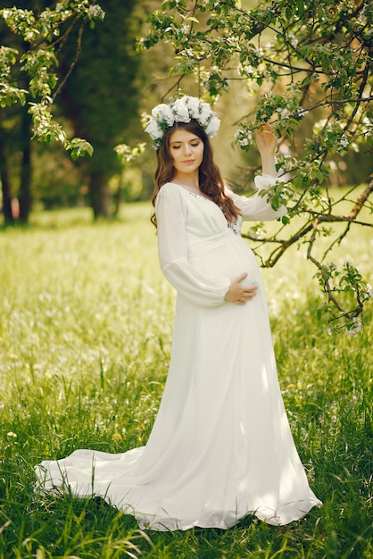 beautiful young pregnant girl in a long white dress and wreath on her head 