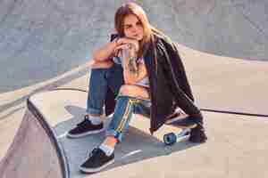 Free photo beautiful young skater girl trendy dressed sitting on longboard at skatepark.