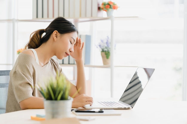 Beautiful young smiling asian woman working laptop on desk in living room at home