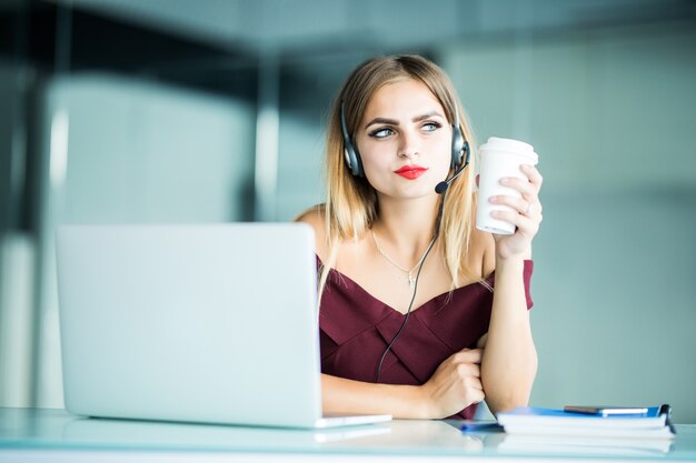 Beautiful young smiling woman with headphones and cup of coffee looking in office