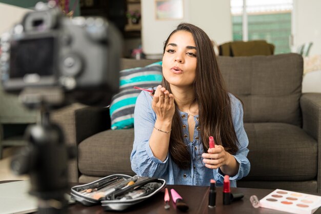 Beautiful young woman blowing a kiss to a camera while recording a video blog about beauty and makeup