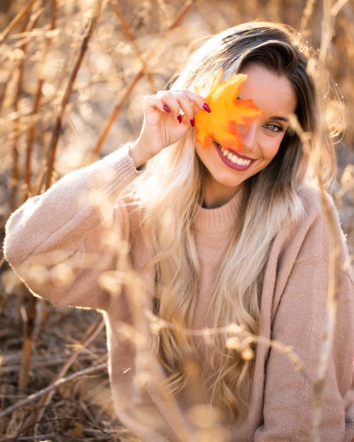 Free photo beautiful young woman blowing maple leaves looking at camera