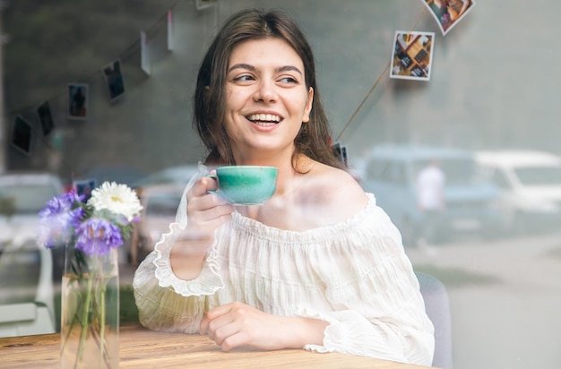 Beautiful young woman in a cafe with a cup of coffee view from the street