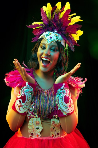 Beautiful young woman in carnival mask and masquerade costume in colorful lights