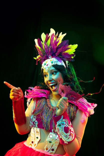 Beautiful young woman in carnival mask and masquerade costume in colorful lights