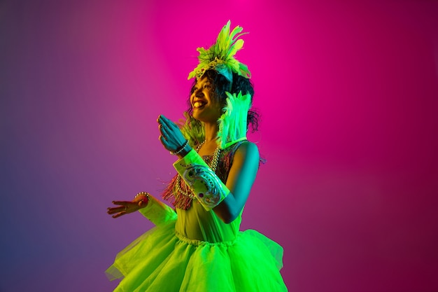 Free Photo beautiful young woman in carnival, stylish masquerade costume with feathers dancing on gradient wall in neon