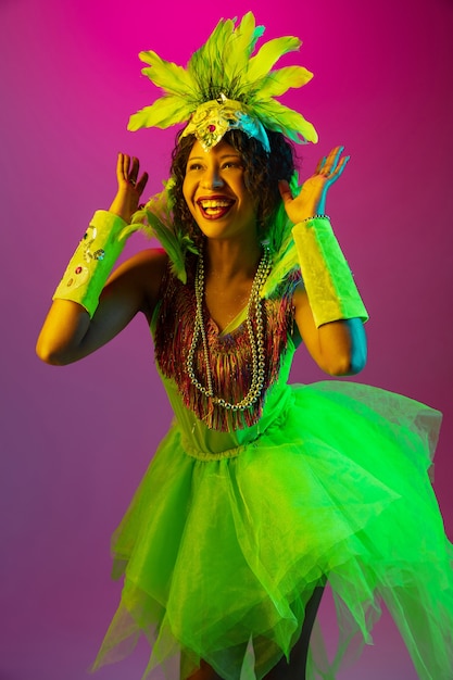 Free Photo beautiful young woman in carnival, stylish masquerade costume with feathers dancing on gradient wall in neon