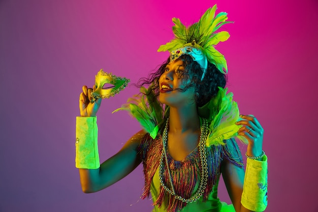 Free Photo beautiful young woman in carnival, stylish masquerade costume with feathers dancing on gradient wall in neon