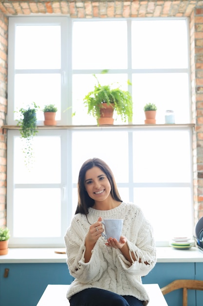 Free photo beautiful young woman drinking a hot drink in the kitchen