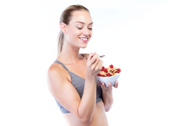 Beautiful young woman eating cereals and fruits over white background.