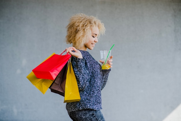 Free photo beautiful young woman holding beverage and bags