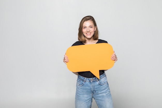 Free photo beautiful young woman holding blank speech bubble over grey wall