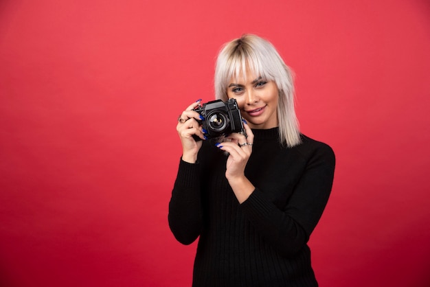 Free photo beautiful young woman holding a camera while standing against red background. high quality photo