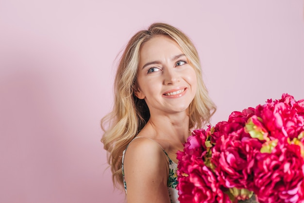 Beautiful young woman holding rose bouquet against pink background