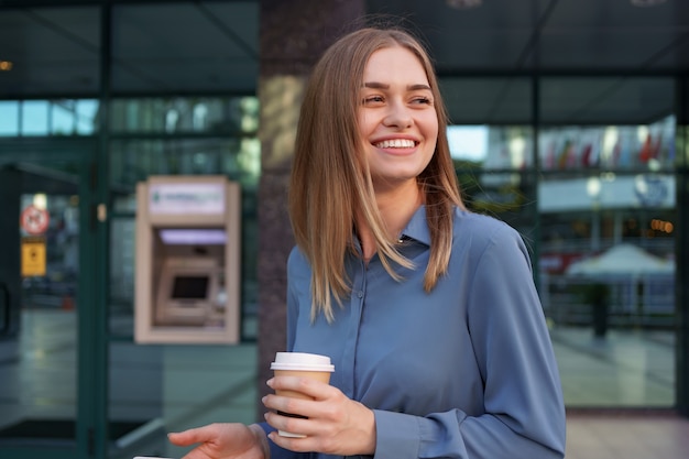 Beautiful young woman is using an app in her smartphone device to send a text message near business buildings