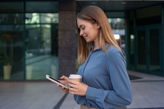 Beautiful young woman is using an app in her smartphone device to send a text message near business buildings