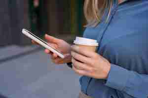 Free photo beautiful young woman is using an app in her smartphone device to send a text message near business buildings