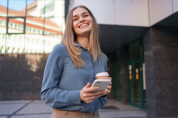 Beautiful young woman is using an app in her smartphone device to send a text message near business buildings