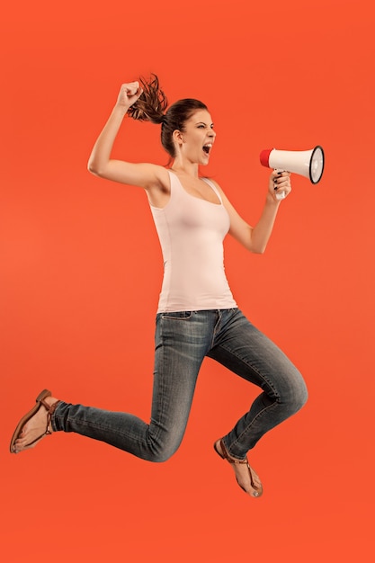 Free Photo beautiful young woman jumping with megaphone isolated over red background. runnin girl in motion or movement. human emotions and facial expressions concept