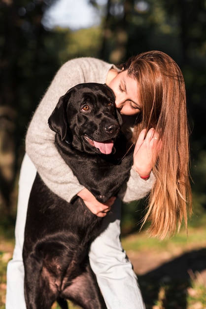 Free Photo beautiful young woman kissing her black labrador in park