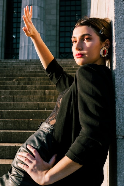 Free photo beautiful young woman leaning on wall shielding her eyes from sun