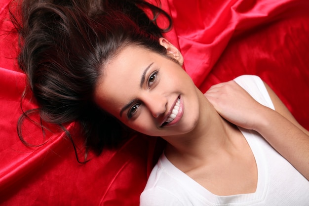 Beautiful young woman lying in red silk, top view