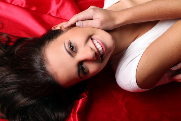 Beautiful young woman lying in red silk, top view