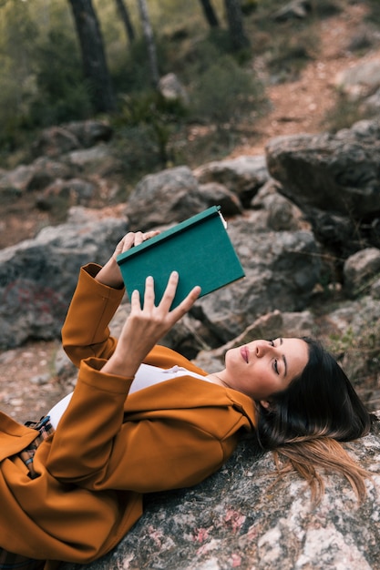 Free Photo beautiful young woman lying on the rock reading the book