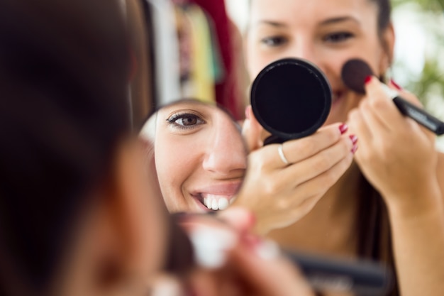 Beautiful young woman making make-up near mirror at home.