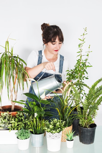 Beautiful young woman pouring water on potted plants with watering can