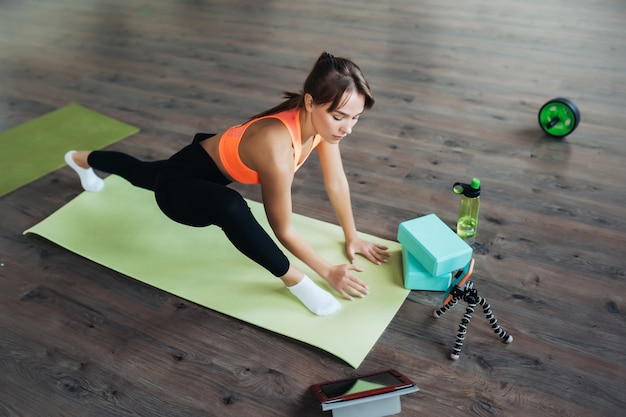 Beautiful young woman practicing yoga, is engaged with the teacher online via a tablet. Home sports concept.