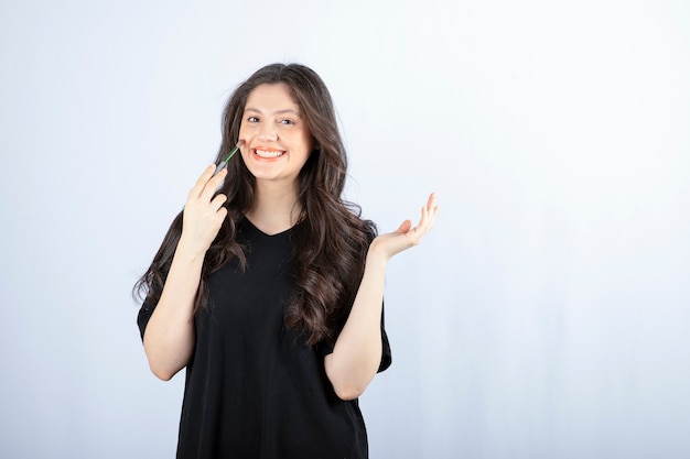 Beautiful young woman putting blush with cosmetic brush over white wall.