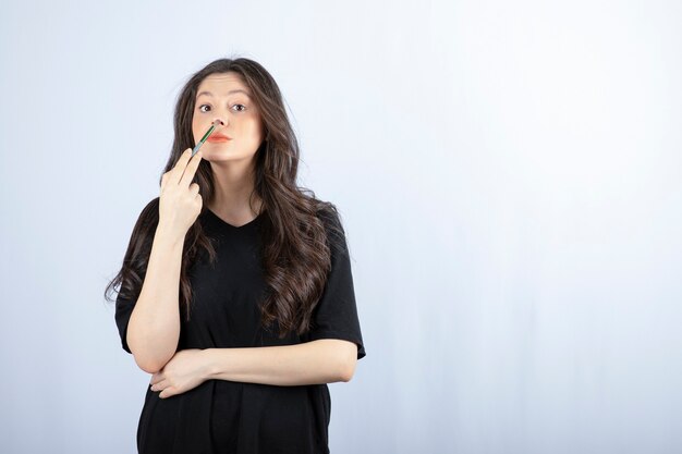 Beautiful young woman putting highlighter with cosmetic brush to her nose.