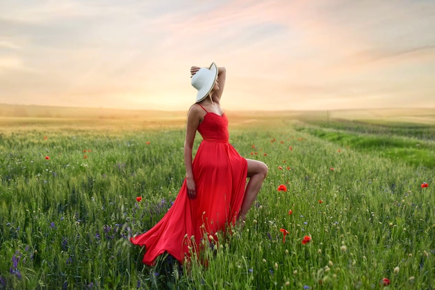 Free photo beautiful young woman in red dress and white hat walks around field with poppies