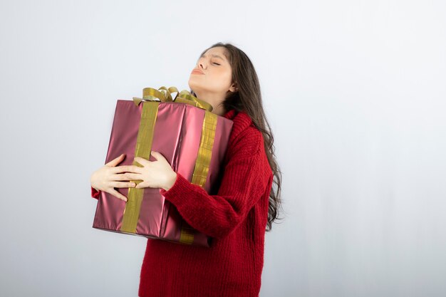 Beautiful young woman in red sweater standing and holding gift box.. 